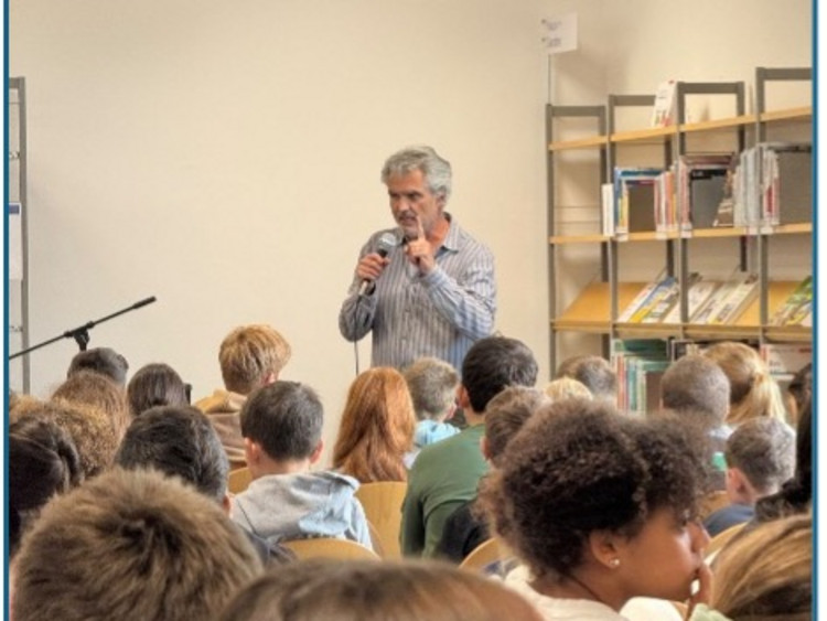 Mann steht am Mikrofon, Schüler sitzen im kreis darum herum