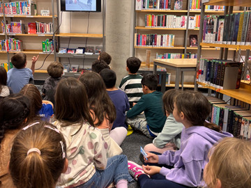 Kinder sitzen auf dem Boden der Bücherei und hören zu